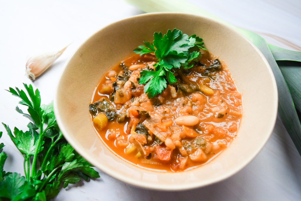 large bowl of tuscan bean soup with brilliant green parsley and a long cove of garlic